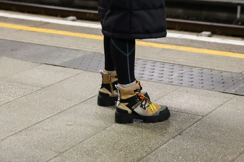 Brown hiking boots with colorful laces on train platform with gray concrete tiles