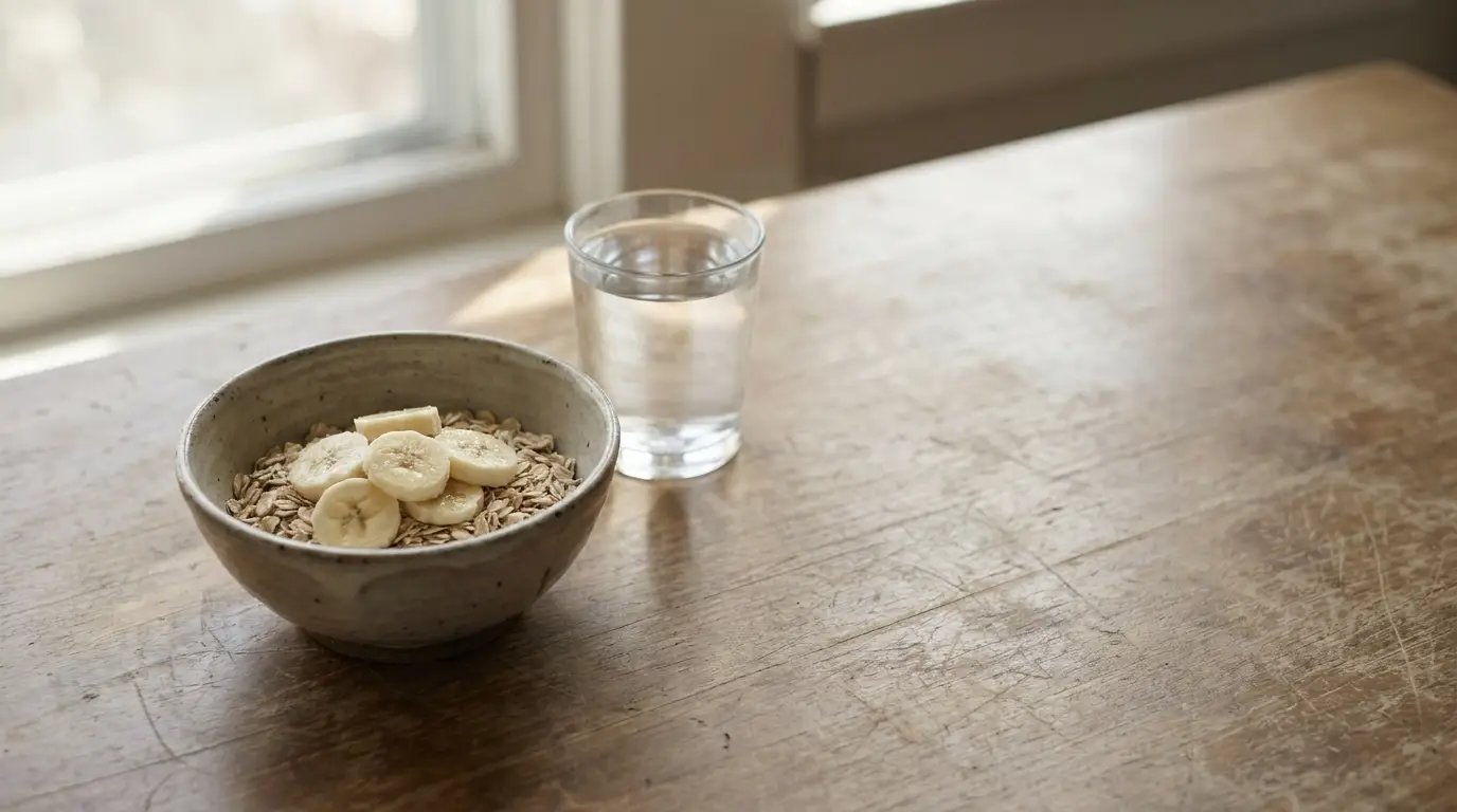 Bowl of oatmeal with banana slices and a glass of water on wooden table