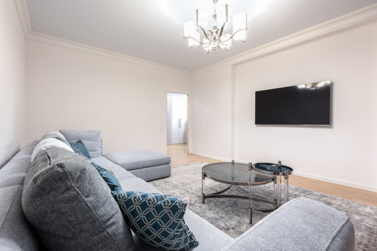 Gray sectional sofa and glass coffee table in a modern living room with chandelier