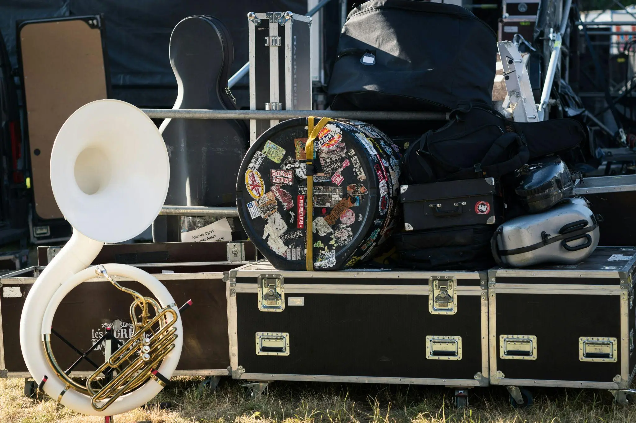 White sousaphone and instrument cases stacked outdoors at a music festival stage setup