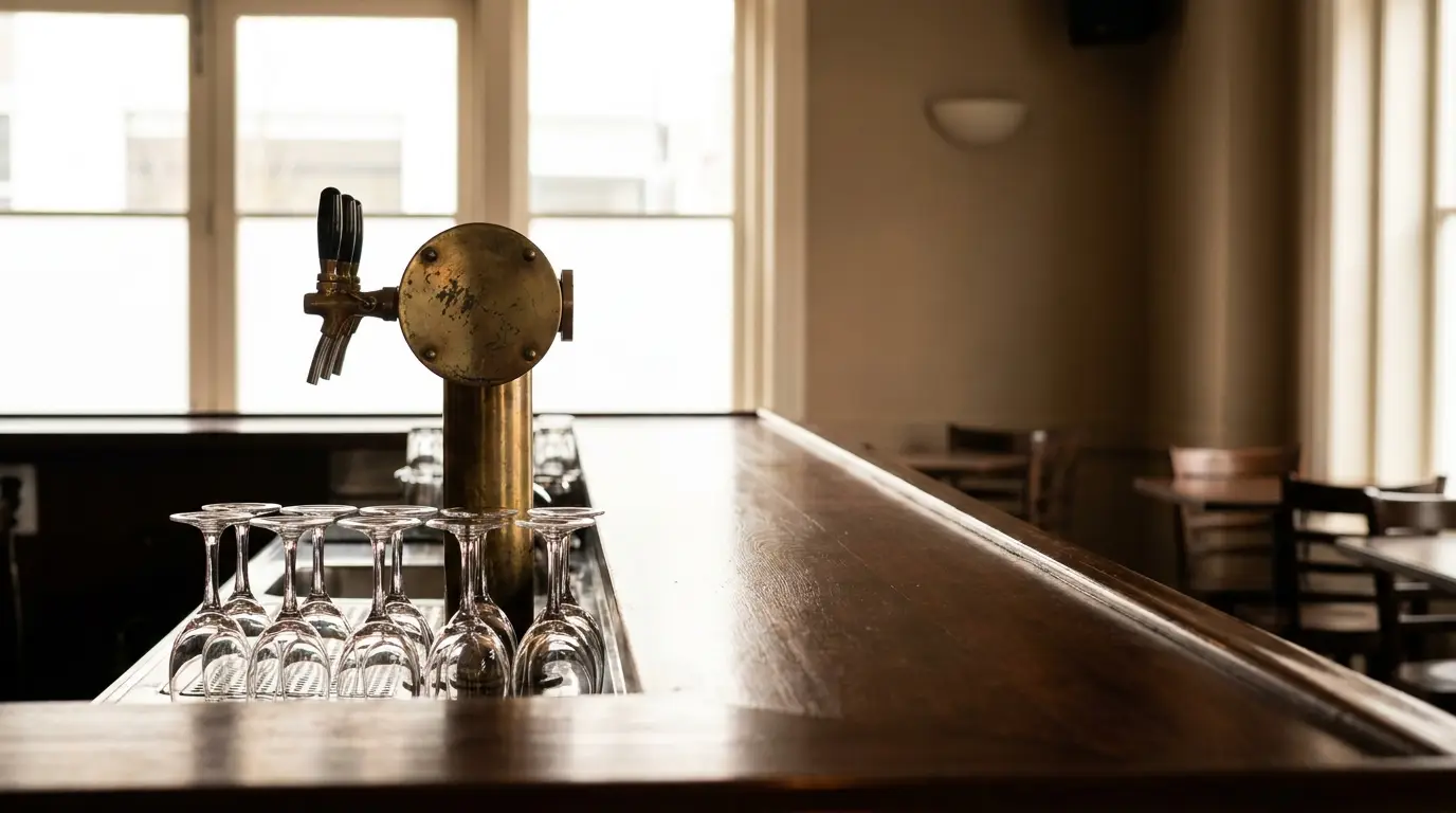 Brass beer tap and upside-down glasses on wooden bar counter in dimly lit pub