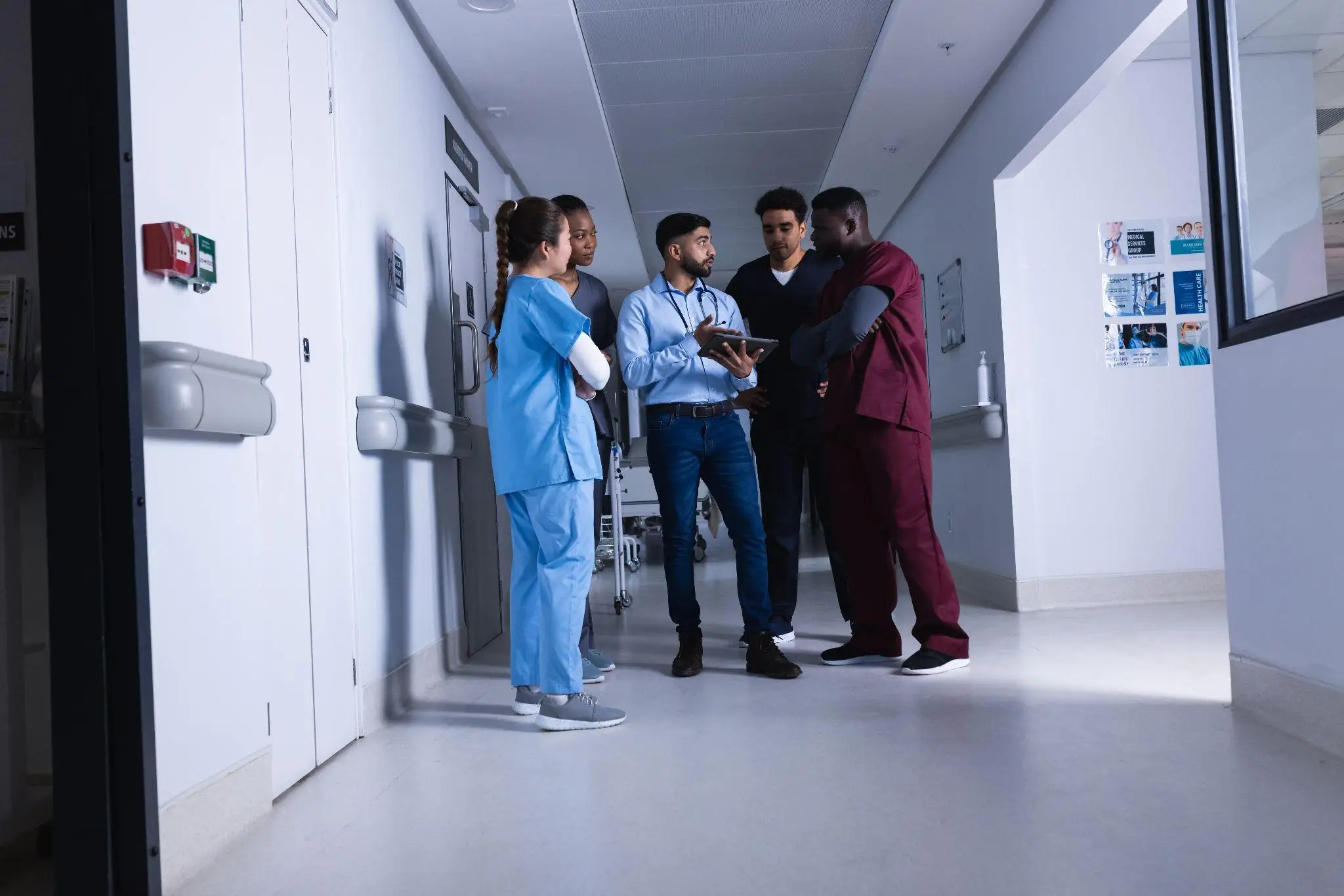 Medical team discussing with tablet in a hospital corridor under bright lighting