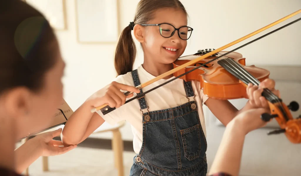Girl playing violin with guidance from teacher in cozy indoor setting