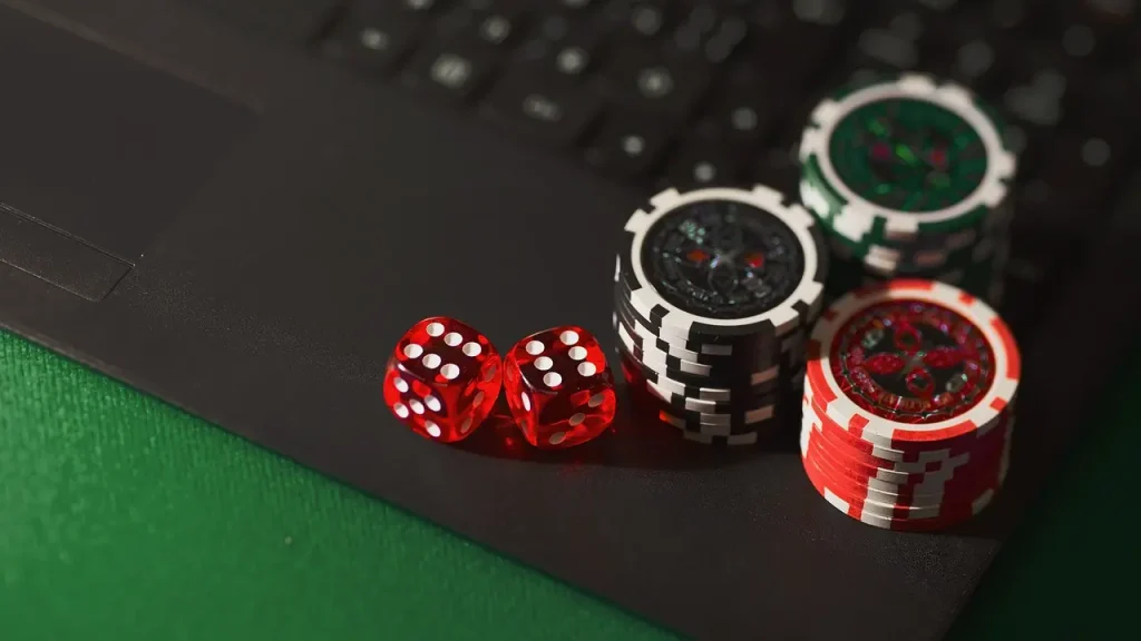 Poker chips and red dice on a black laptop keyboard with green felt background