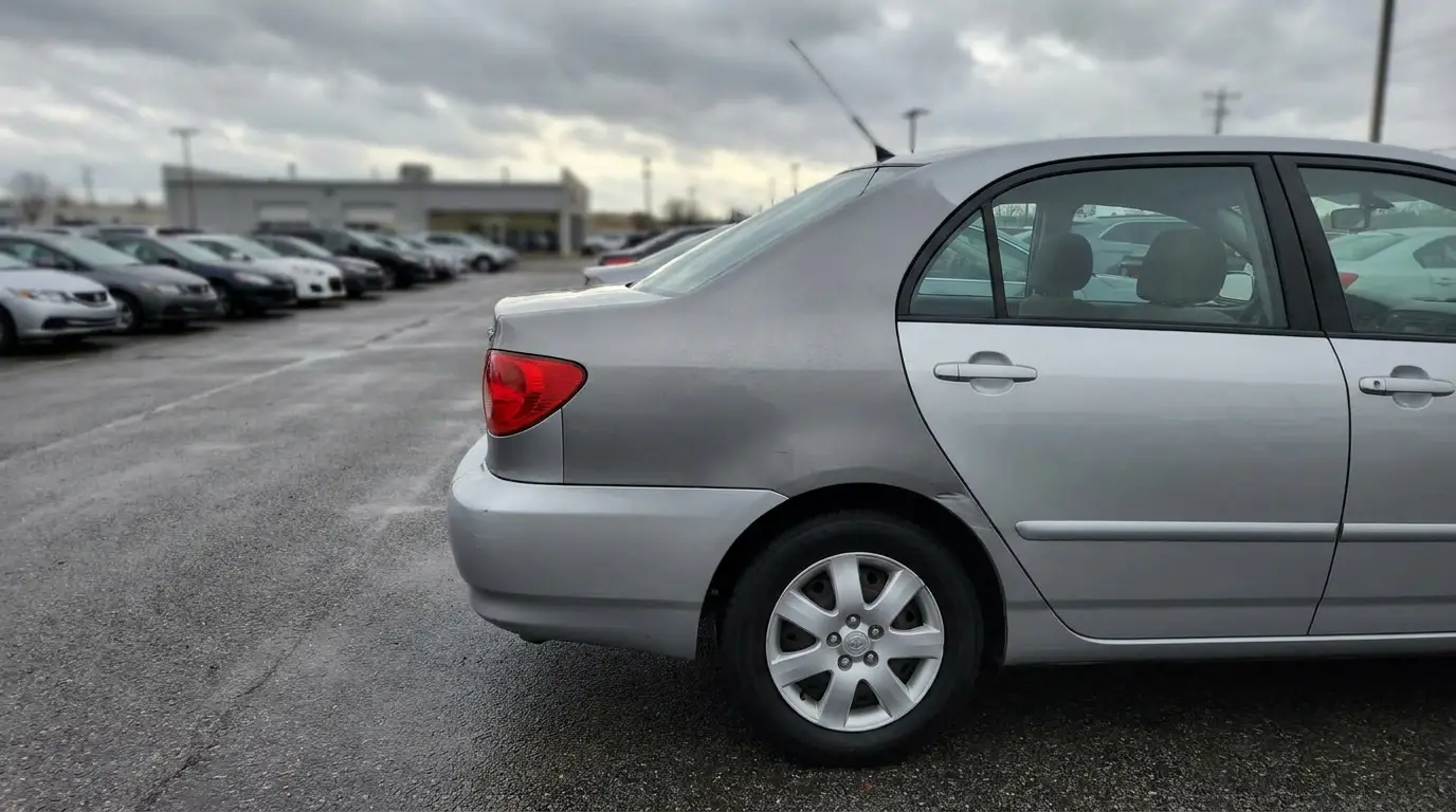 Silver sedan parked in outdoor car dealership lot under cloudy sky