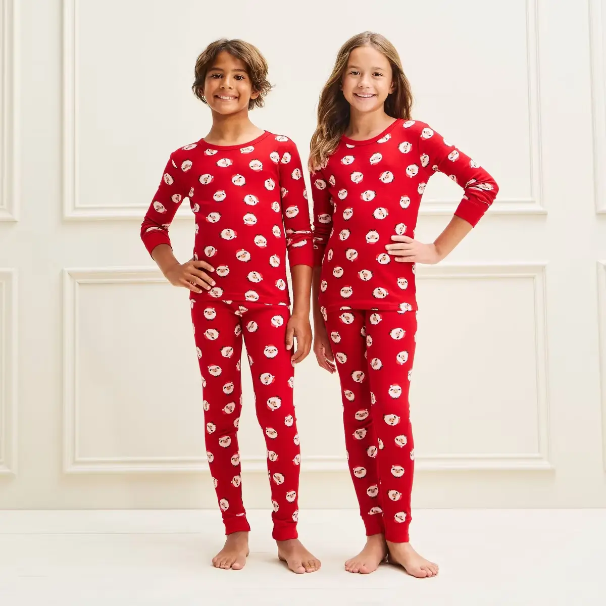 Two children wearing matching red Santa pajamas standing in a light-colored room