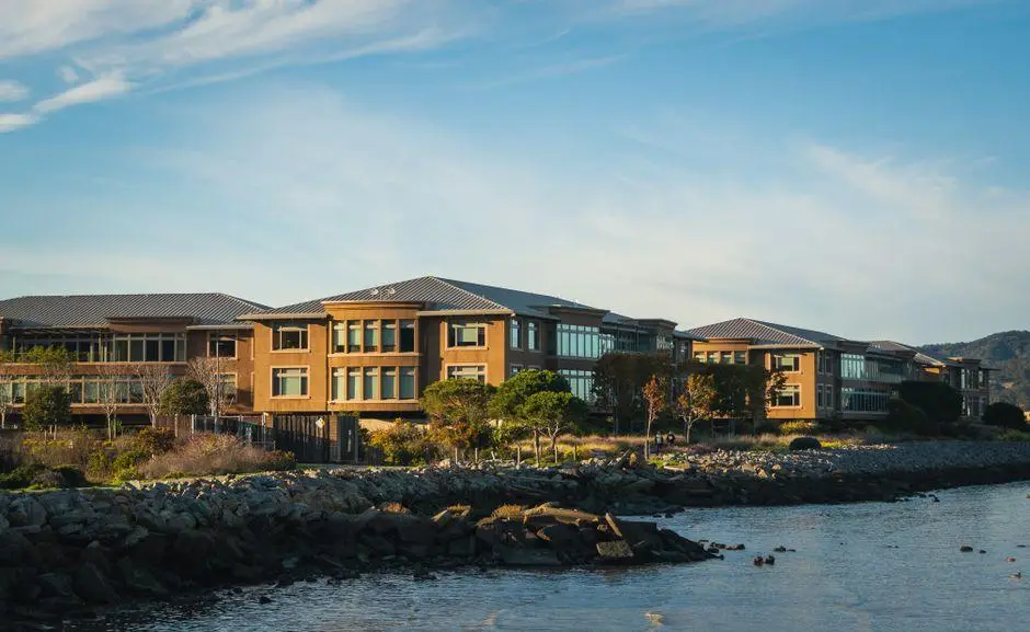 Large modern buildings with glass windows by rocky shoreline under clear blue sky
