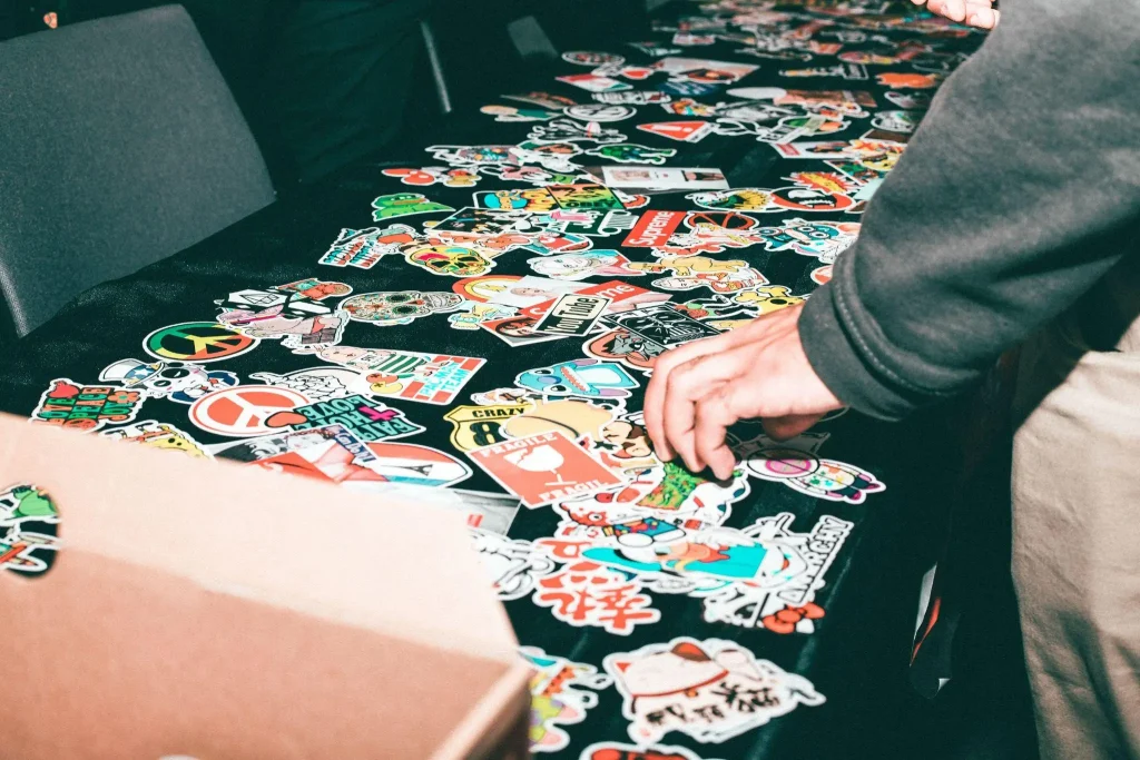 Collection of colorful stickers spread on a black table with a person reaching for one